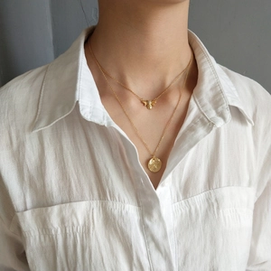 Detail of a layered gold necklace featuring a bee pendant and a hammered metal disc