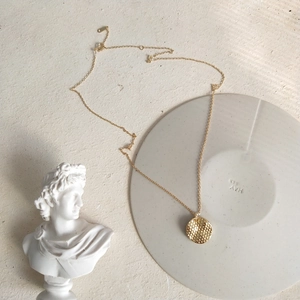 Detailed view of a gold-plated honeycomb textured round pendant necklace on a jewelry tray