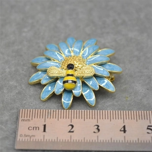 Detail of blue enamel daisy brooch with a bee charm and scale ruler for size reference
