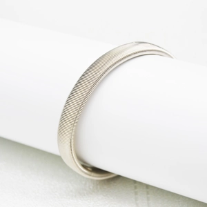 Detailed view of silver metal spring cuff bracelet with fine texture on a white stand