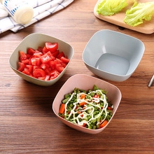 Detailed view of three eco-friendly square bowls in green, gray, and pink on a wood table