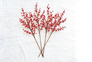 Three vibrant red faux holly berry stems on a soft white plush faux fur background