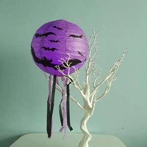 Detail of purple Halloween paper lantern with bat prints and hanging ribbons on a tree