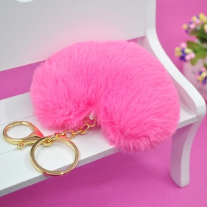 Llavero de corazón de peluche rosa con aro dorado sobre un banco decorativo