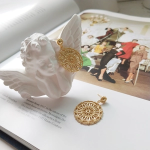 Artistic close-up of gold hollow circular mandala earrings next to a white angel statue
