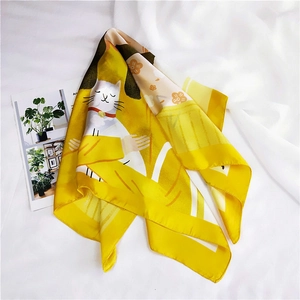 Detailed view of yellow silk scarf featuring cartoon white cat and orange floral patterns