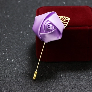 Detail of a purple ribbon rose brooch with golden metal leaves and long pin on black glitter