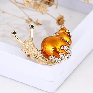 Macro detail of snail brooch with orange enamel shell and sparkling crystals on gold alloy