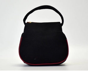 Front view of a minimalist black canvas handbag featuring red piping and top handle
