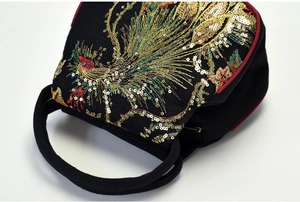 Close-up of intricate gold and green phoenix embroidery with sequins on black fabric bag