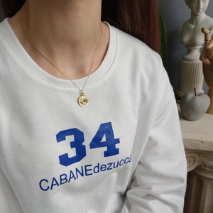 Close-up of vintage gold coin pendant necklace worn on a white sweatshirt