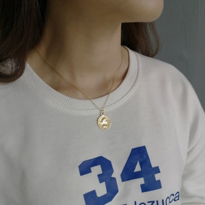 Close-up of golden coin pendant necklace on model wearing a white printed sweatshirt