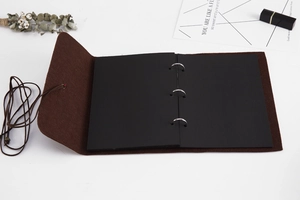 Detail view of open brown felt DIY photo album with black pages and metal binder rings