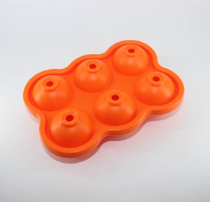 Detail view of an orange silicone ice ball mold with six spherical slots on white background