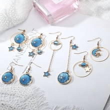 Detailed close-up of blue celestial star and moon drop earrings on elegant lace fabric