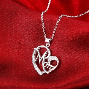 Détail macro du pendentif cœur MOM serti de zircons sur fond de satin rouge élégant