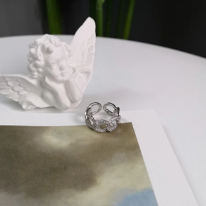 Artistic close-up of a silver chain ring with pavé zircons next to a mini statue