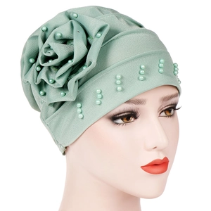 Detail of light green turban hat featuring a 3D fabric flower and elegant pearl beads