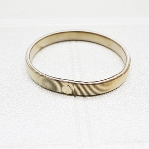 Close-up of golden metal spring armband with round decorative buckle on textured white base