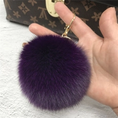 Macro shot of fluffy purple mink fur pompom keychain with golden metal clasp