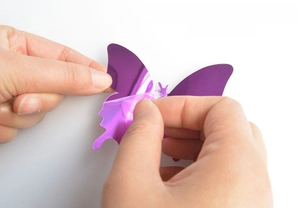 Close-up showing the removal of protective film from purple 3D mirror butterfly wall sticker