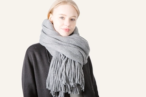 Close-up of thick grey faux wool scarf with long tassels draped on a black coat