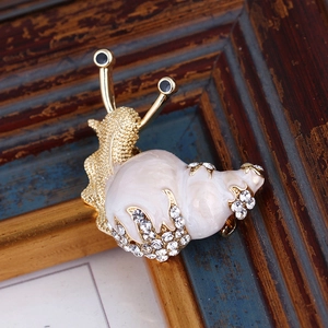 Macro shot of an elegant gold snail brooch with white pearls and sparkling crystals