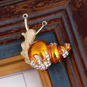 Detailed view of snail brooch with amber-like shell and rhinestones on wood