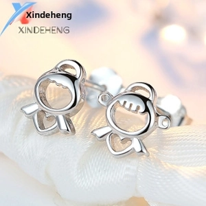 Macro shot of silver cartoon girl stud earrings with heart detail on white silk background