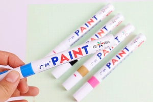 Close-up of hand holding a blue permanent paint marker from a six-color set