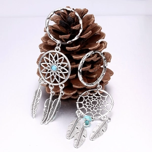Silver dreamcatcher earrings with blue beads and feathers displayed on a pine cone