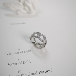 Macro detail of silver chain link ring with pavé zircons on an open art book page