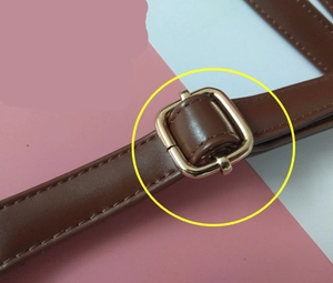 Detail of brown PU leather shoulder strap with golden metal buckle and stitching
