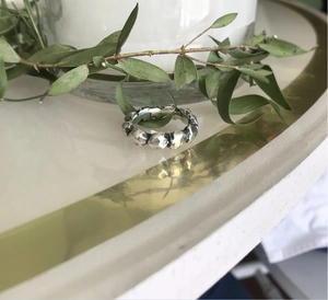 Close-up of silver ring with hammered metal texture on white surface with green leaves