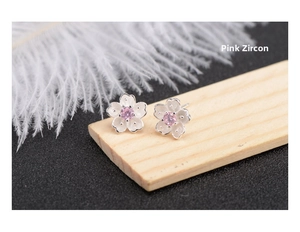 Close-up of cherry blossom stud earrings with pink zircon on a wooden surface
