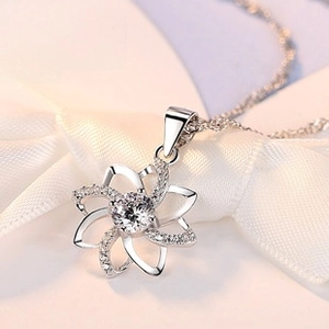 Macro shot of a silver petal pendant necklace with sparkling zircons on white silk