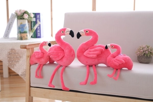 Detail of pink flamingo plush toys in two sizes on a grey sofa in a cozy home setting