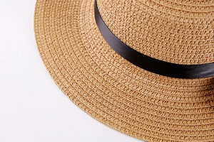 Detailed close-up of woven straw texture and black silk ribbon on flat top sun hat