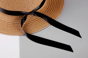 Detail of woven straw sun hat texture featuring elegant black satin ribbon bow