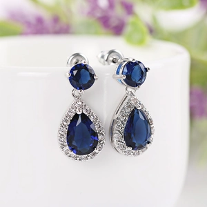 Macro detail of dark blue pear-cut zircon earrings with silver settings on a white cup