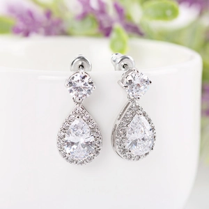 Detail of teardrop zircon earrings with silver plating hanging on a white porcelain cup