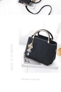Detail einer schwarzen Lederhandtasche mit goldenem Griff und elegantem Kristallanhänger