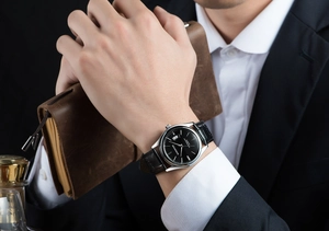 Business style black leather strap watch with silver case on man's wrist in suit