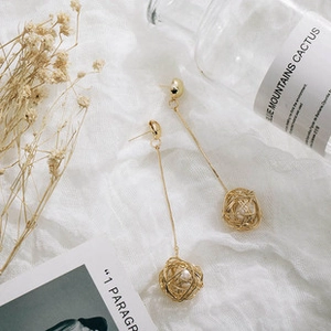 Detailed macro view of long gold twisted wire earrings with white pearl centers on fabric
