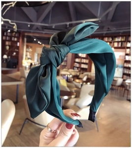 Detailed close-up of a dark green fabric headband with a large handmade satin bow knot