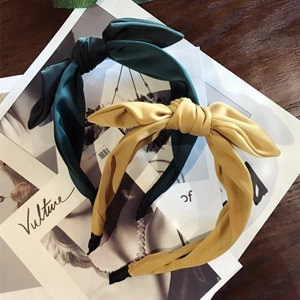 Solid color fabric bow headbands in dark green and yellow on a wooden desk