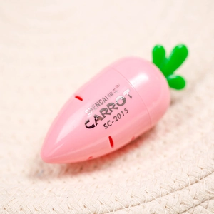 Macro detail of a pink carrot-shaped pencil sharpener with green leaves and silver text