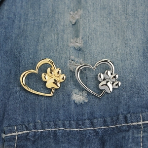 Set of gold and silver heart-shaped paw print pins on blue denim fabric background