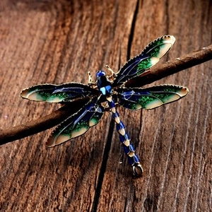 Macro view of blue and green enamel dragonfly brooch on a dark wood branch detail