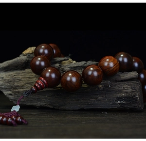 Detail view of Lao Rosewood beads with natural wood grain and red tassel on rustic wood
